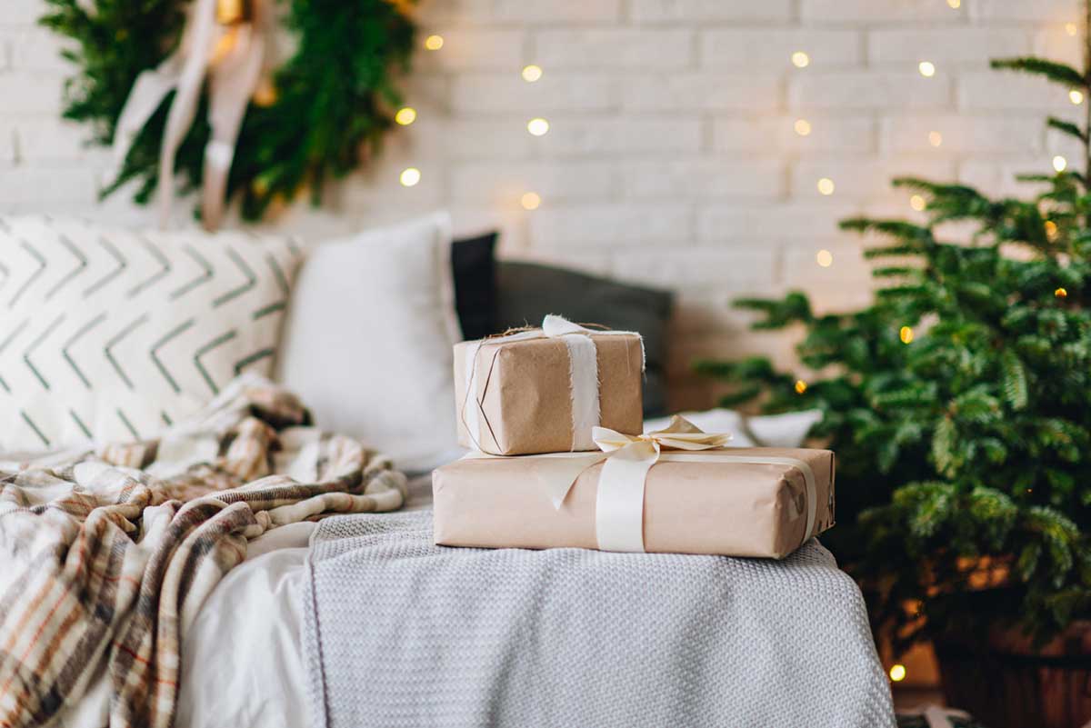 Wrapped Christmas presents on cozy bed next to Christmas tree with beautiful blurred lights on the background. Holiday Eve surprise. Gifts for family and friends during the winter holiday season.